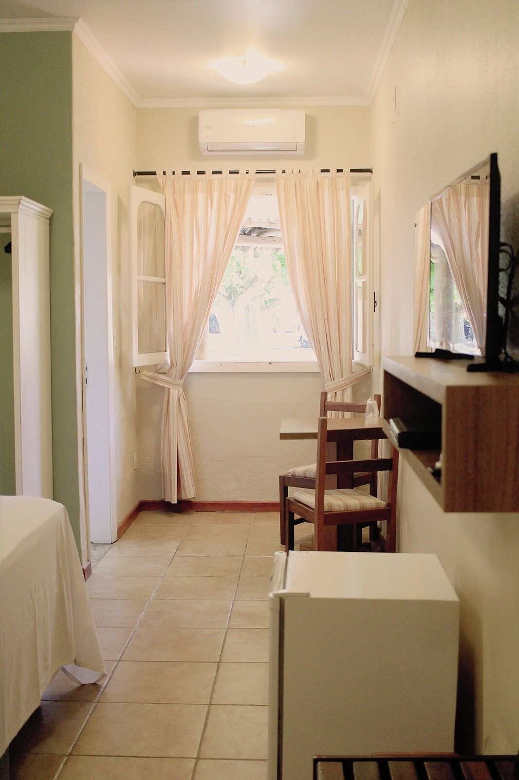 Una habitación pequeña y limpia con cama, silla, escritorio y televisor.