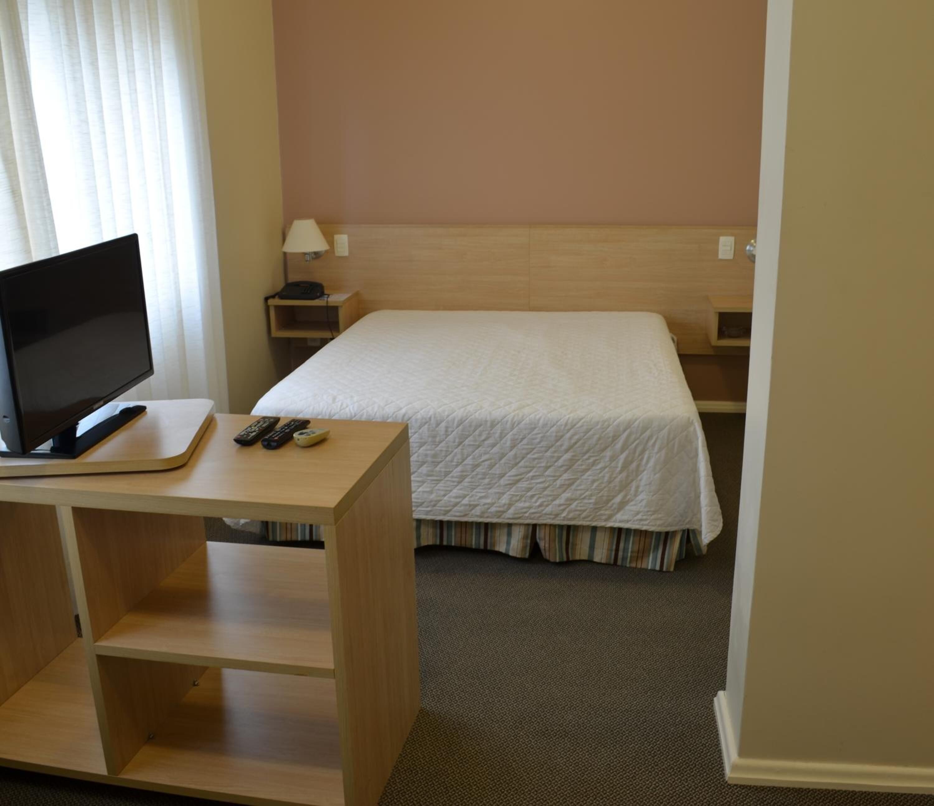 A hotel room with a bed, a desk with a computer, a lamp, and a telephone.