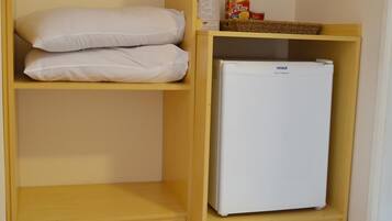 Una pequeña kitchenette con un refrigerador blanco y dos almohadillas blancas en un estante.