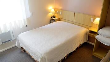 Quarto de hotel com cama grande, abajures, mesa de cabeceira e prateleira embutida.
