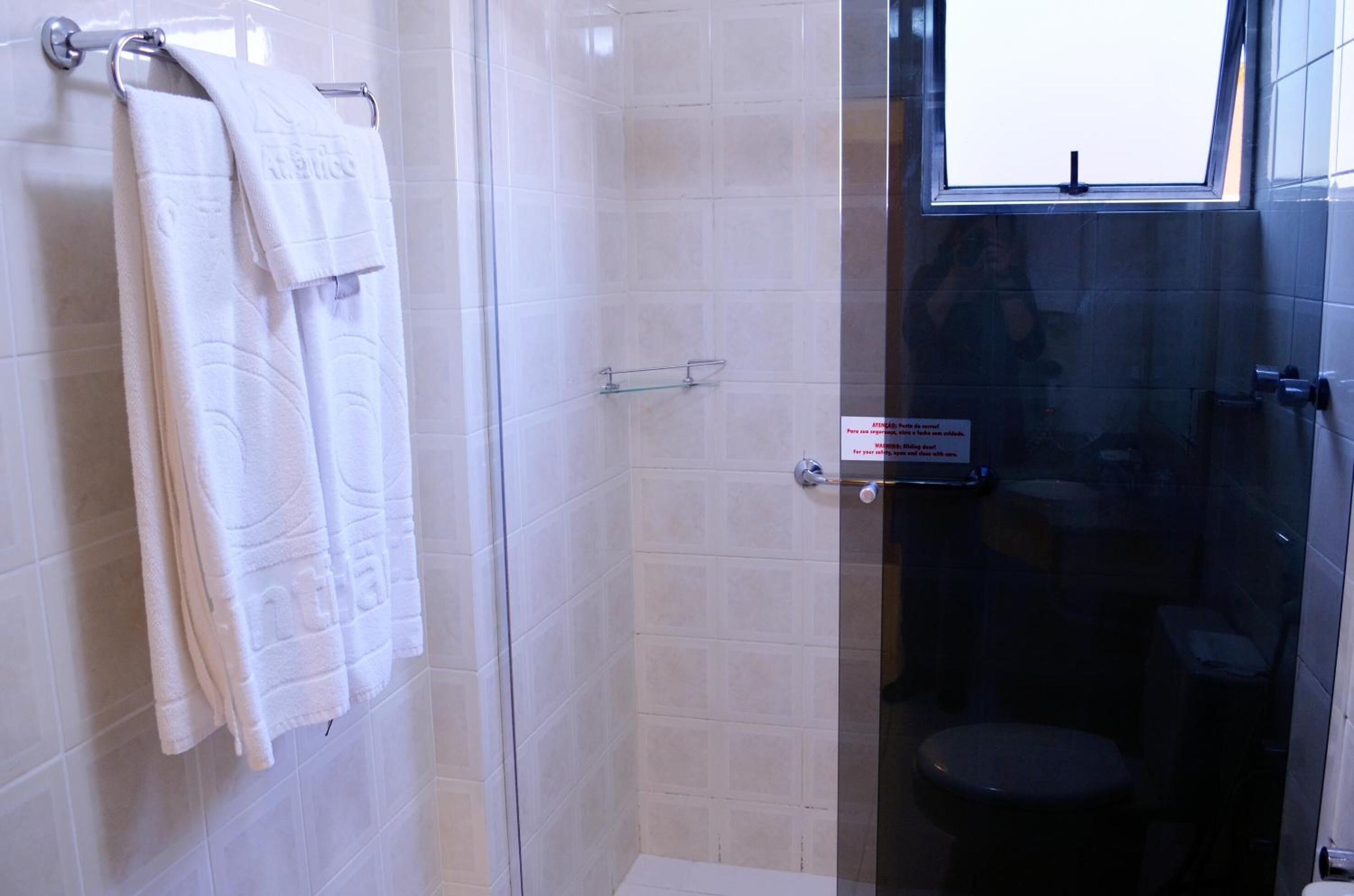 Un baño con cabina de ducha de vidrio, inodoro y toallero con toallas.