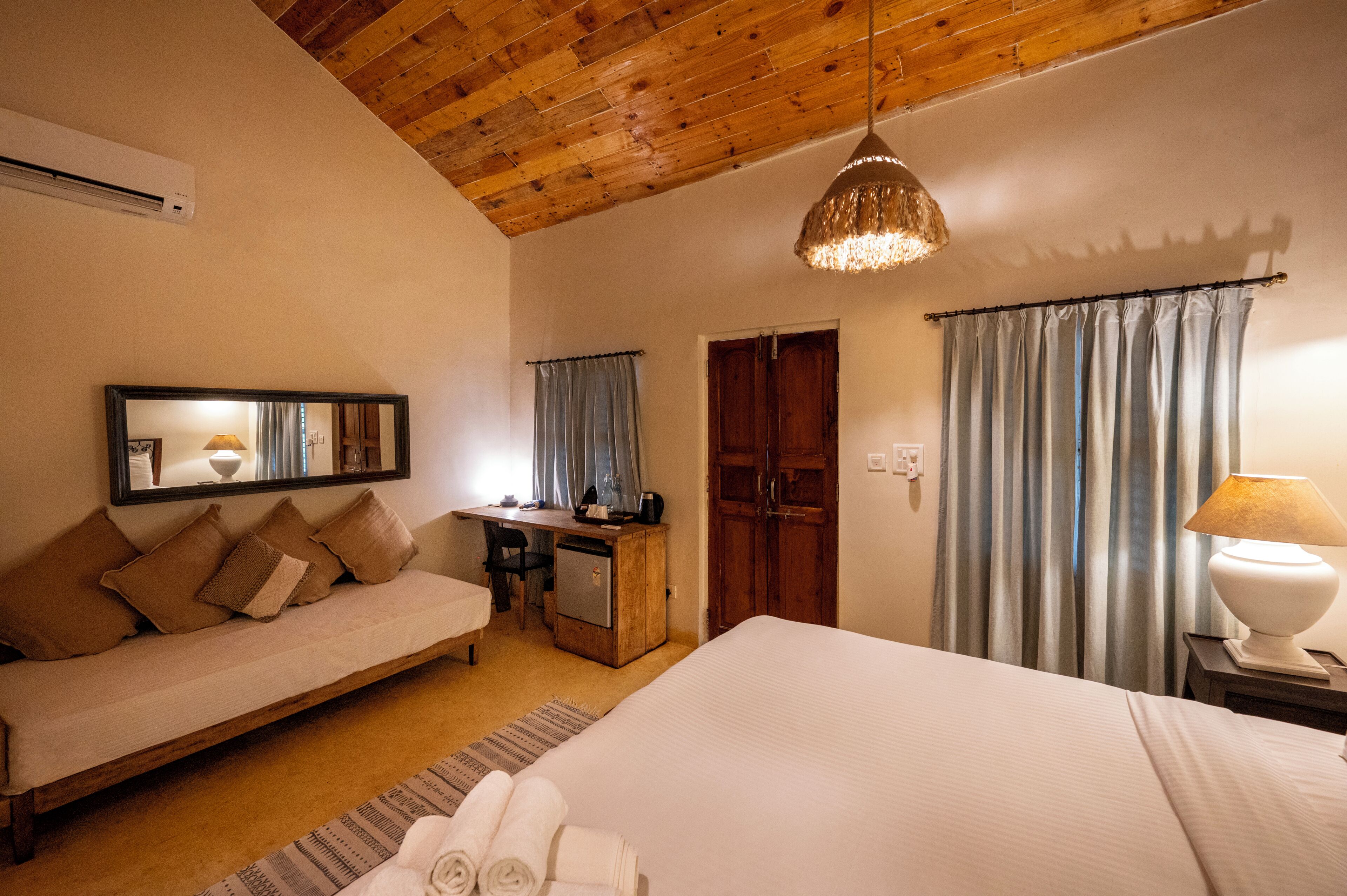 Ein Schlafzimmer mit Bett, Schreibtisch, Sessel, Sofa und einer Pendelleuchte.