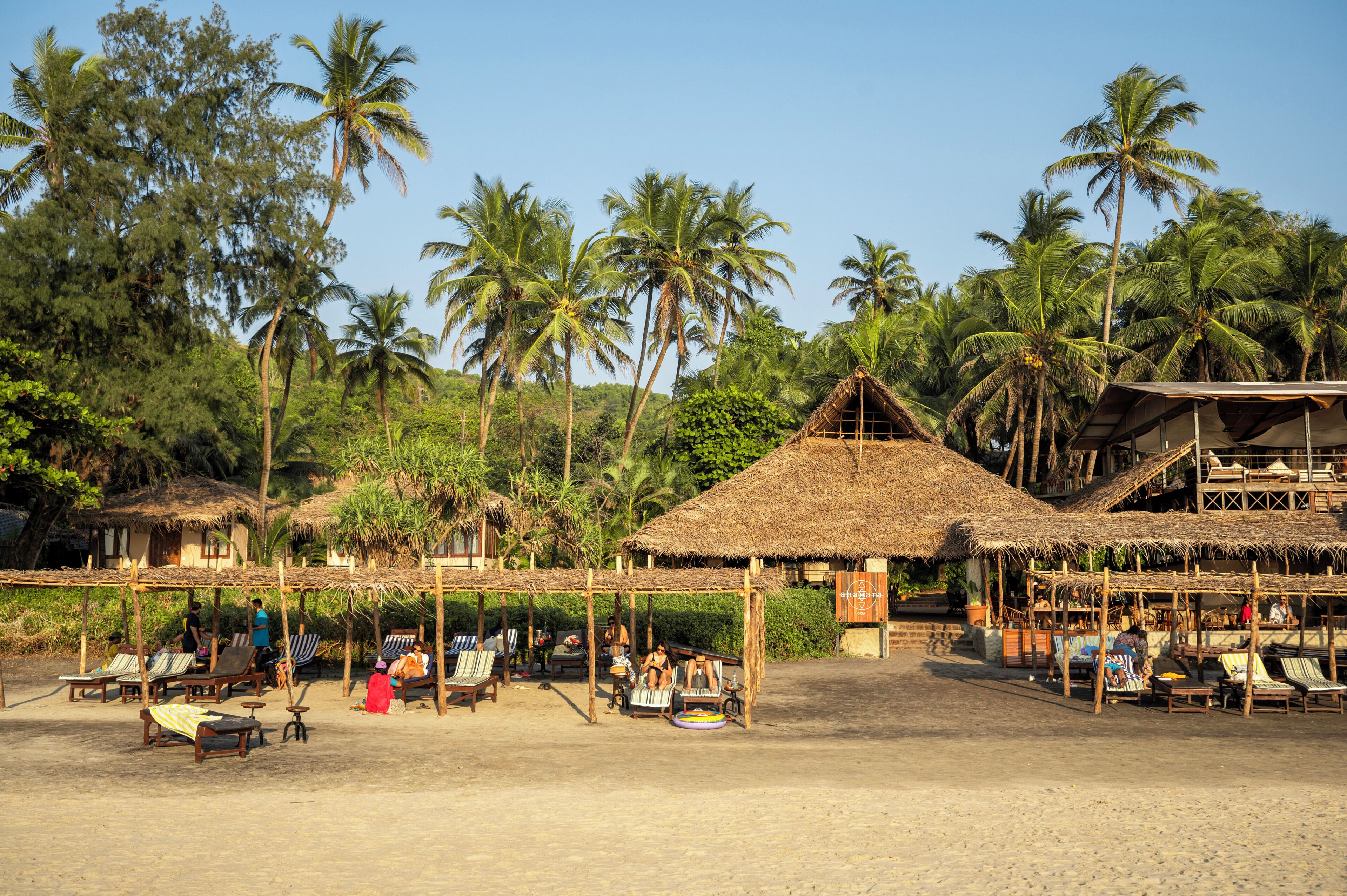 Ein Resort am Strand mit strohgedeckten Hütten, Liegestühlen und Palmen.