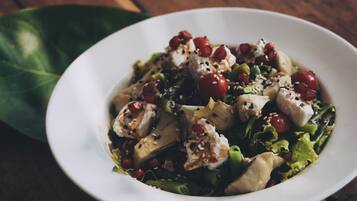 A white bowl of salad with various ingredients, including greens, tomatoes, and sesame seeds, on a wooden table.
