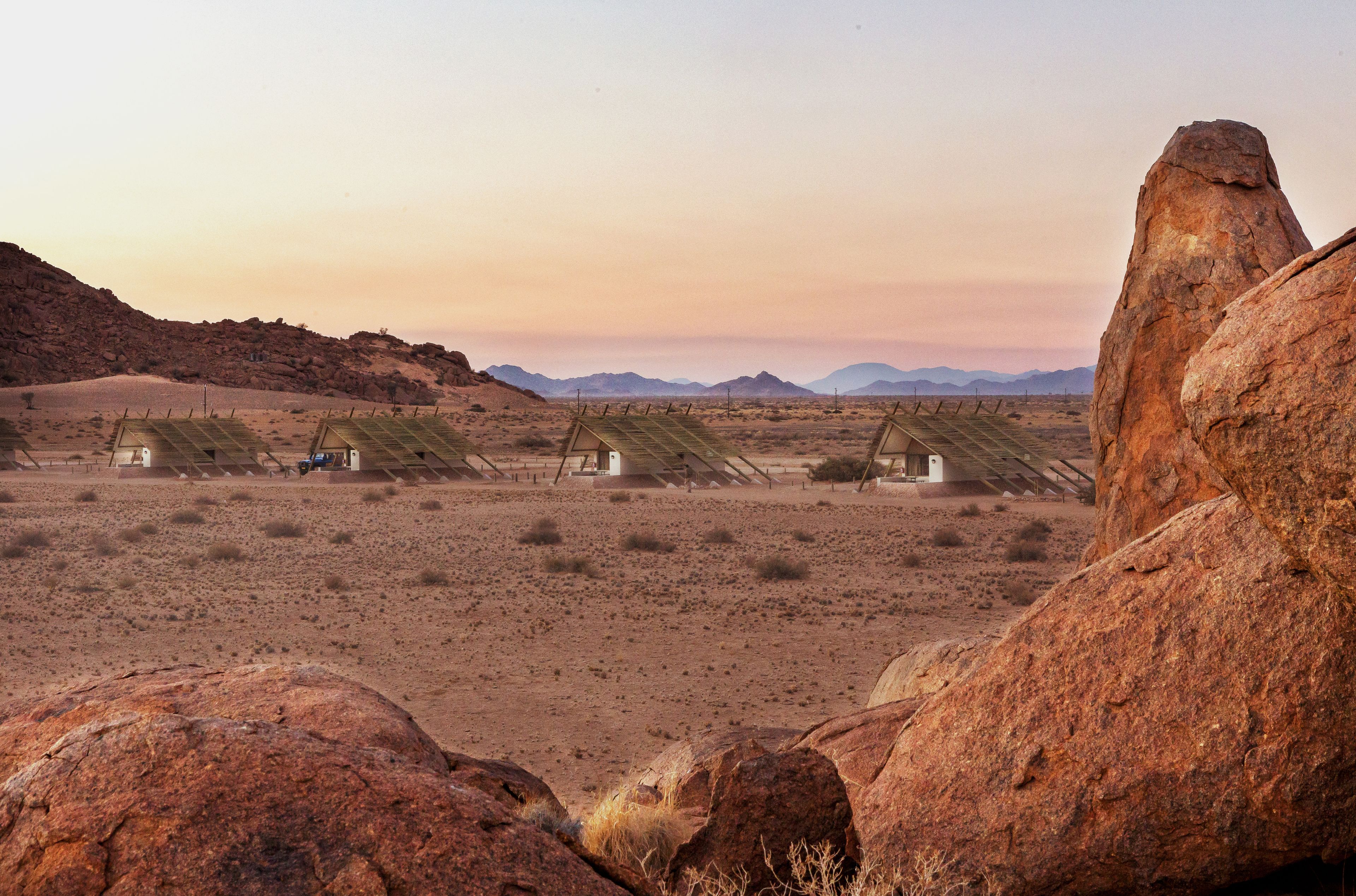 A desert landscape with several tents and a large rock formation.