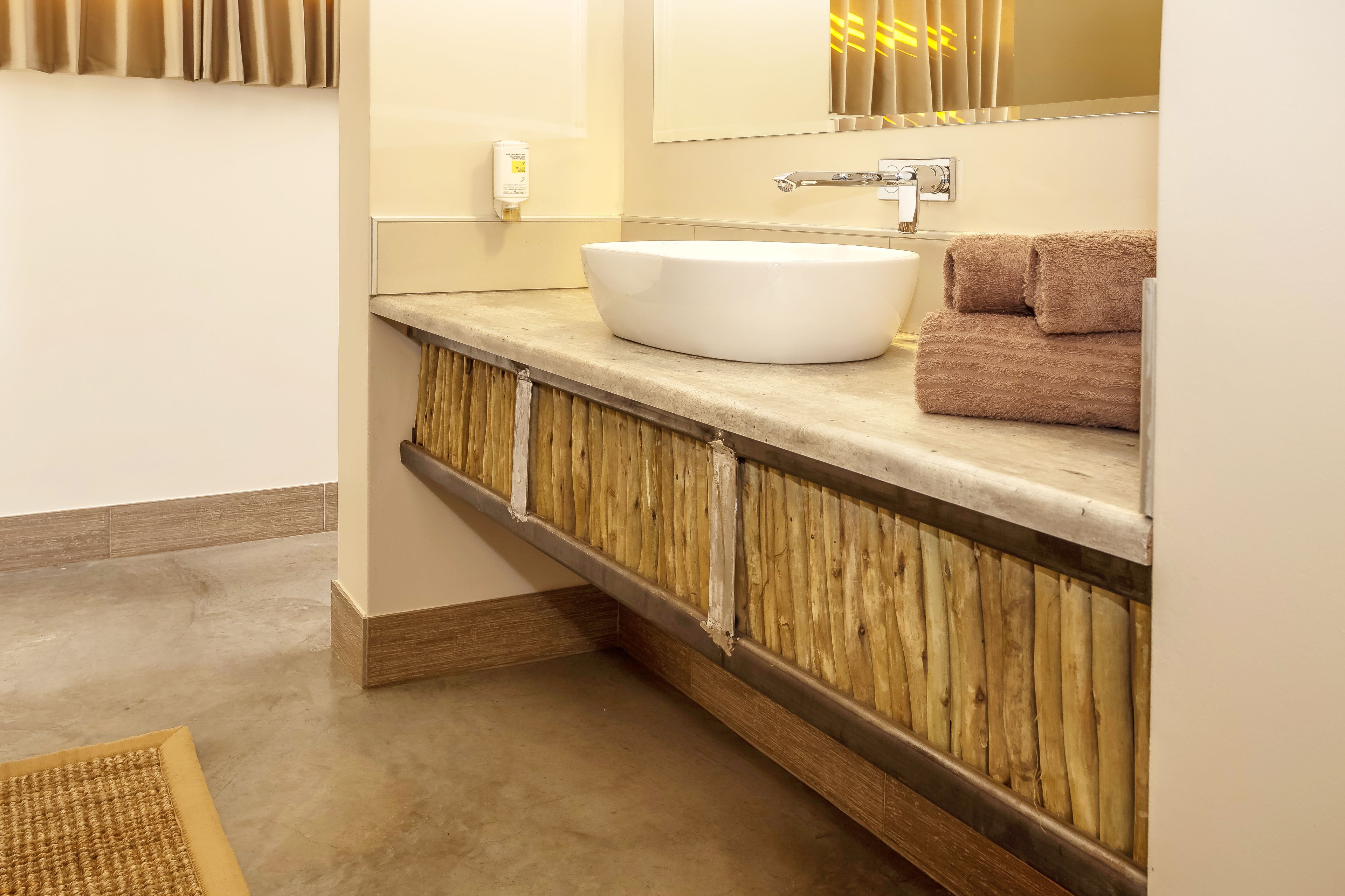 A bathroom with a large white sink, wooden paneling, a towel, and a mirror with a light fixture.