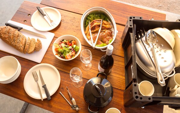 Una mesa de madera dispuesta con platos, cubiertos, hogaza de pan, ensaladera, botella de vino y una olla.