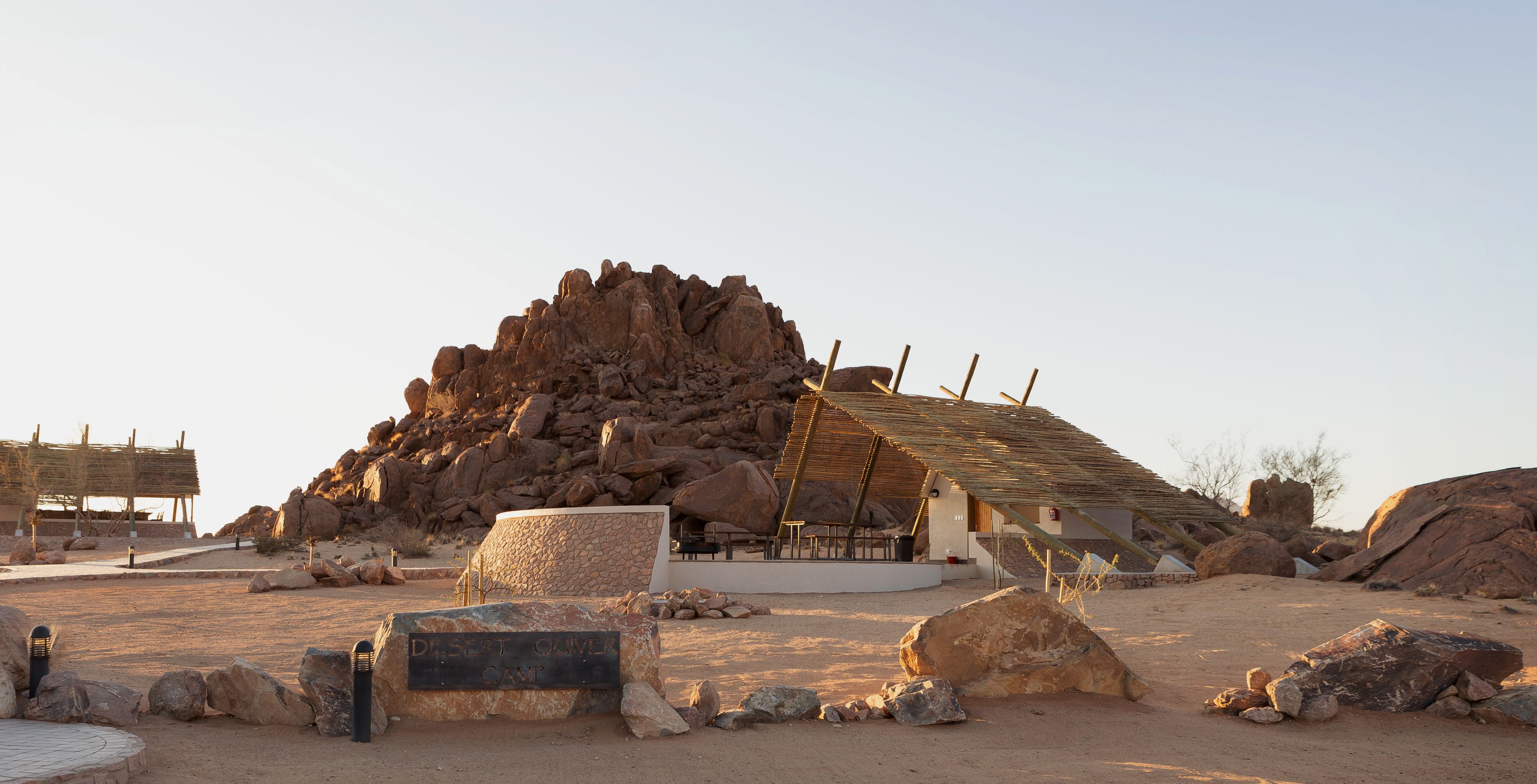 A desert camp with a large rock formation, a thatched-roof structure, and a sign reading "Desert Oasis Camp".