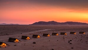 A desert landscape at sunset with multiple small, solar-powered cabins arranged in a row. - Desert Quiver Camp (Sesriem)