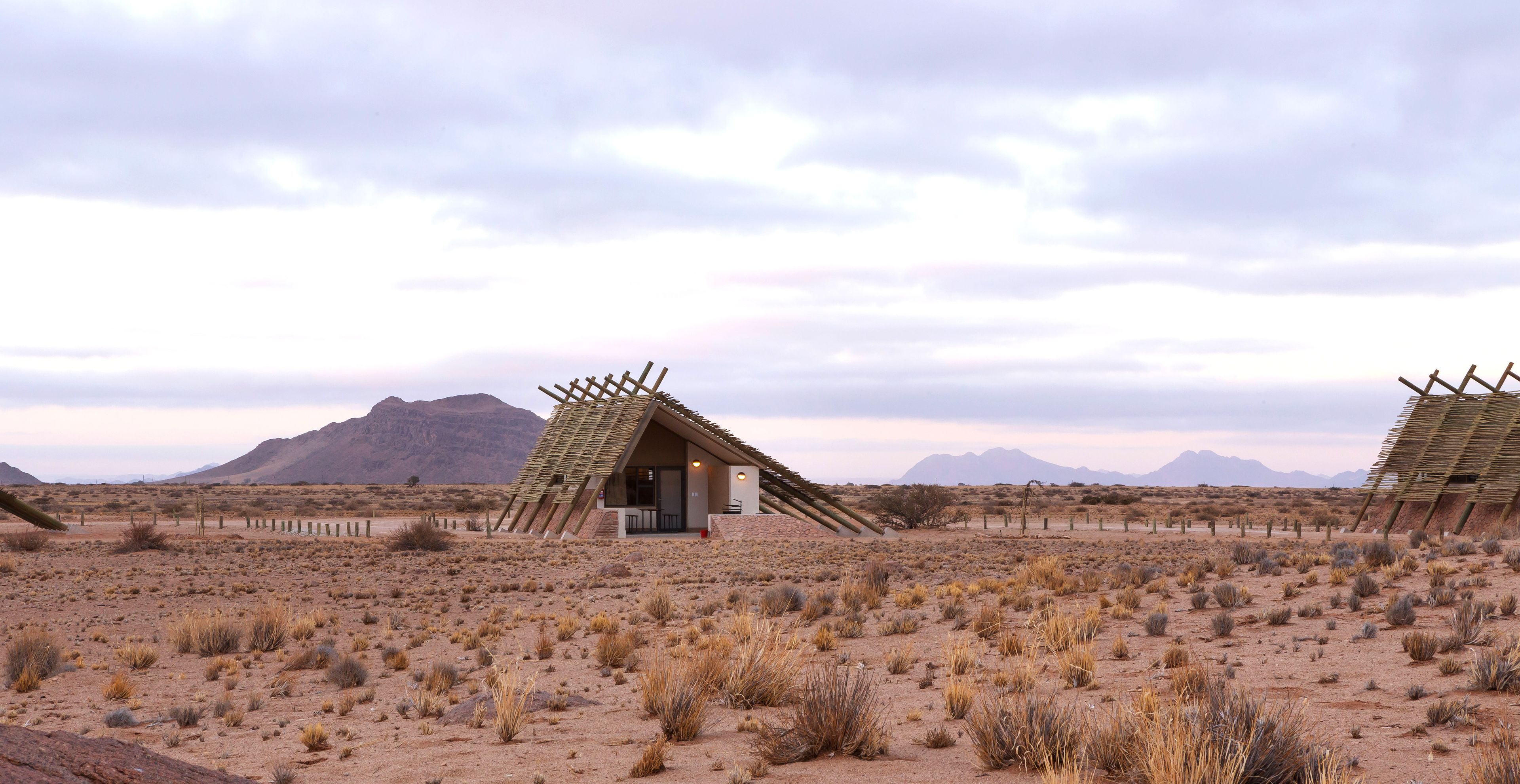 A desert landscape with two wooden structures resembling tents, each with a door and a small porch area.