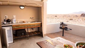 Una kitchenette con pileta, hornalla y espacio de almacenamiento. Hay recipientes con comida y una mesa con vista al desierto.