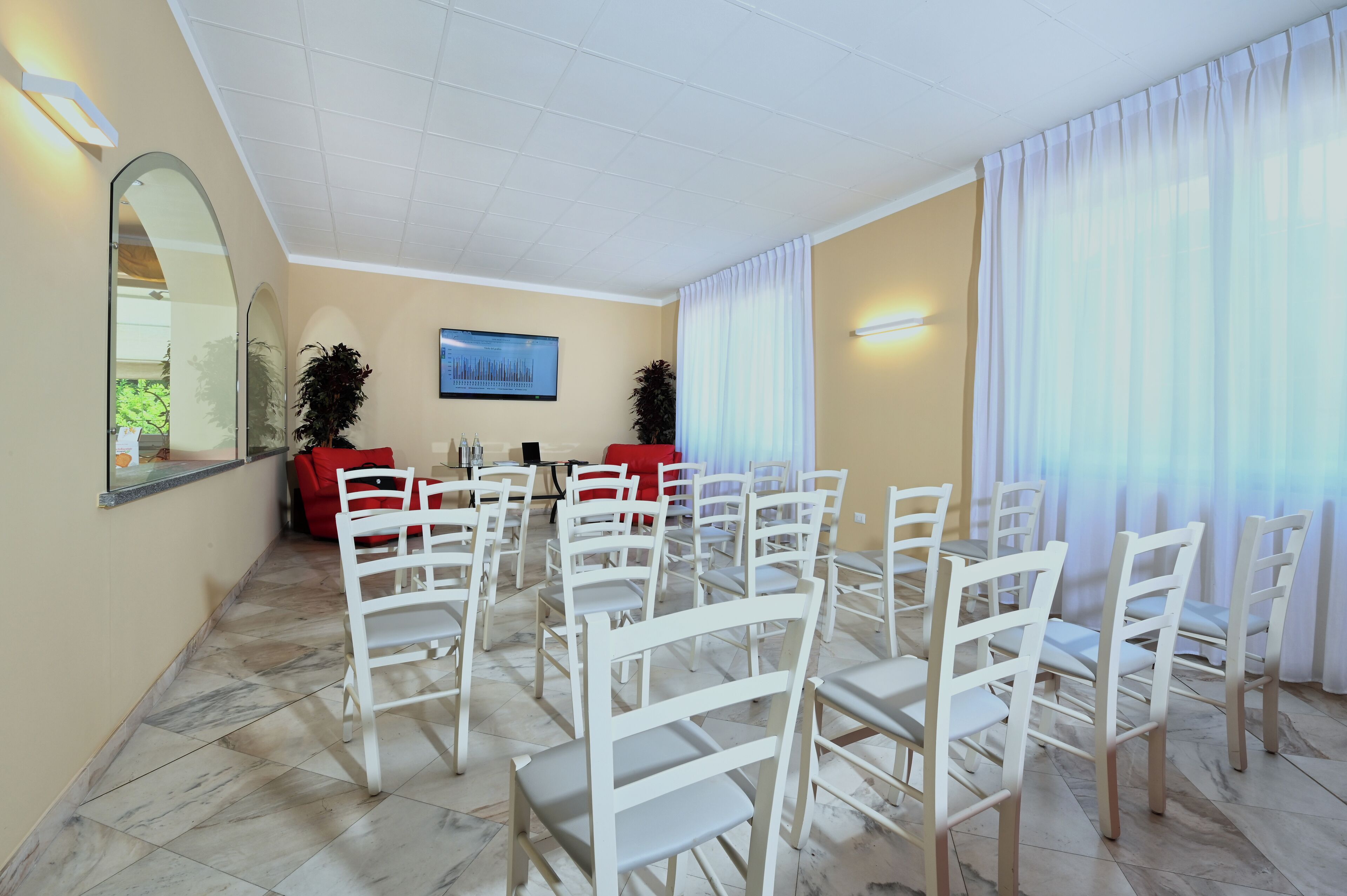 Una sala conferenze con sedie bianche, un divano rosso, un grande specchio e un quadro appeso al muro.