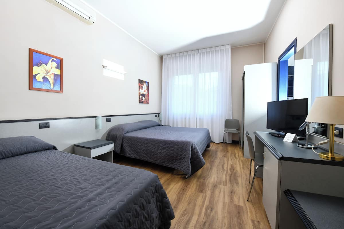 A hotel room with two beds, a desk with a TV, a mirror, and a window with curtains.