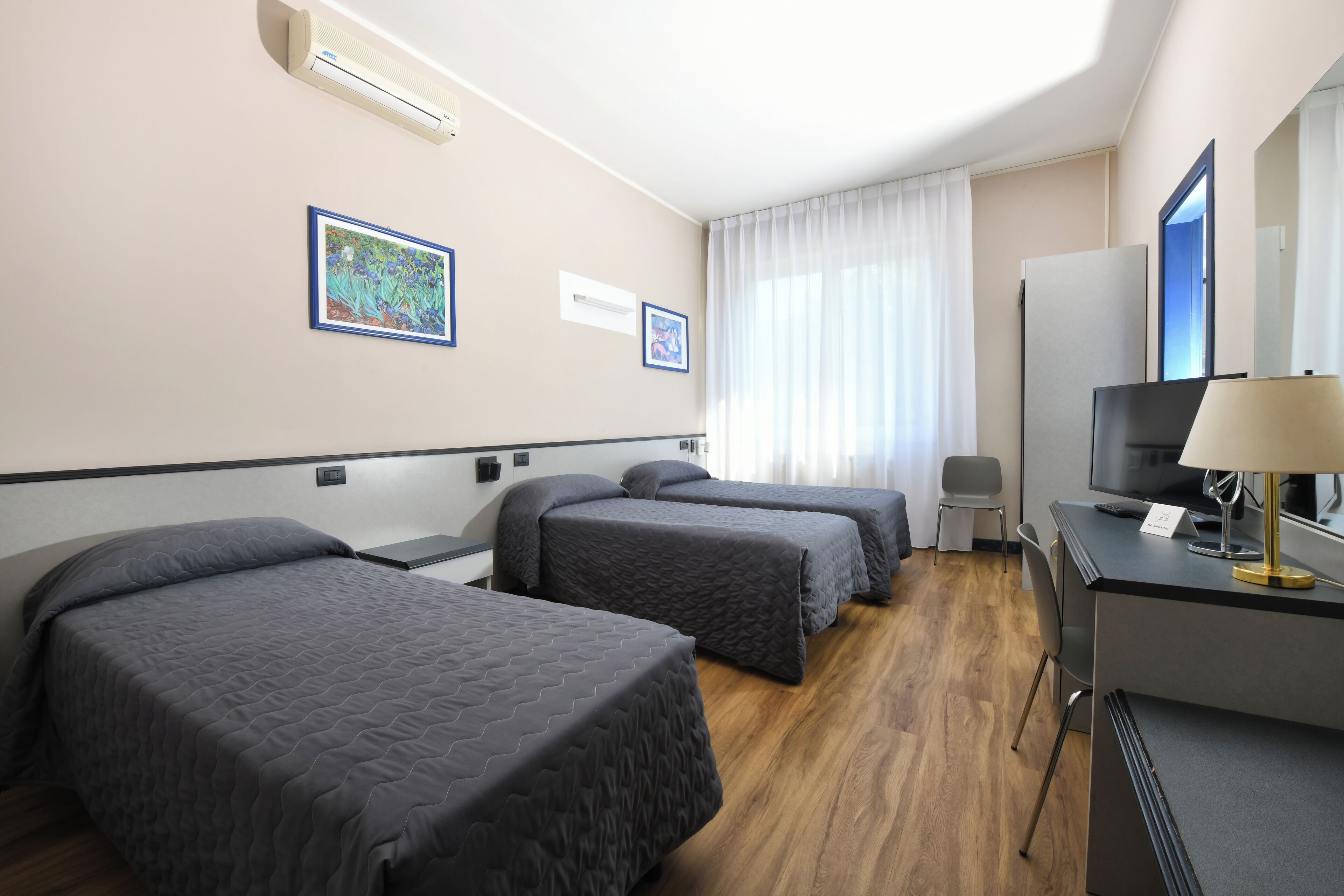 A hotel room with two beds, a desk with a TV, and a window with curtains.