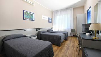 A hotel room with two beds, a desk with a TV, and a window with curtains.
