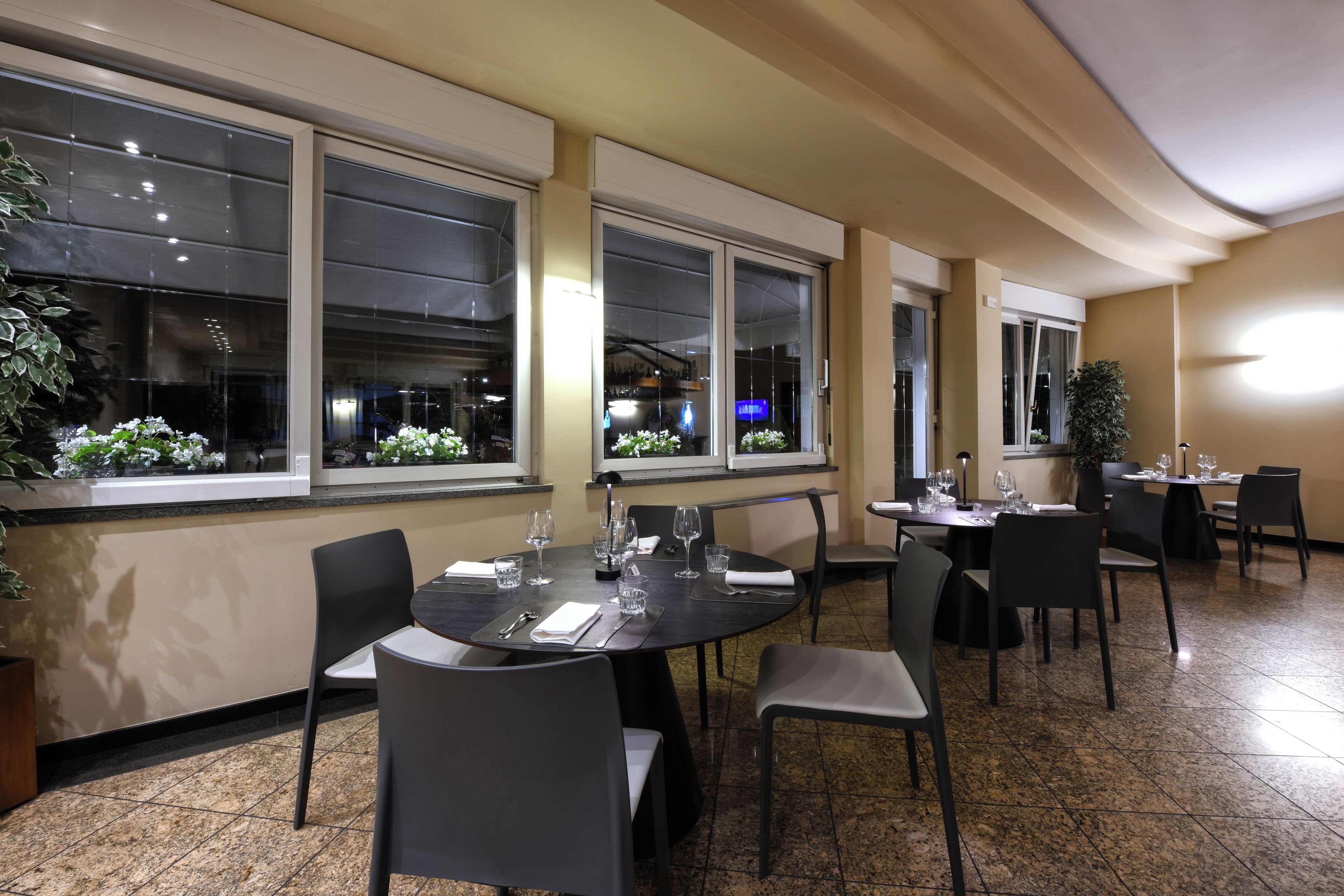 A restaurant with round tables, black chairs, and potted plants.