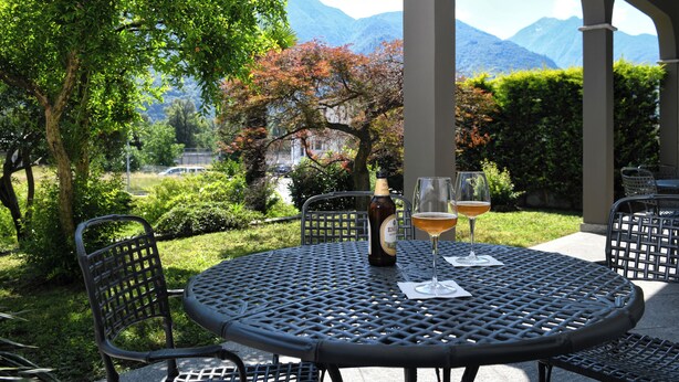 Mesa metálica redonda con dos sillas, una botella de cerveza y dos vasos de cerveza en un patio con vista a la montaña.