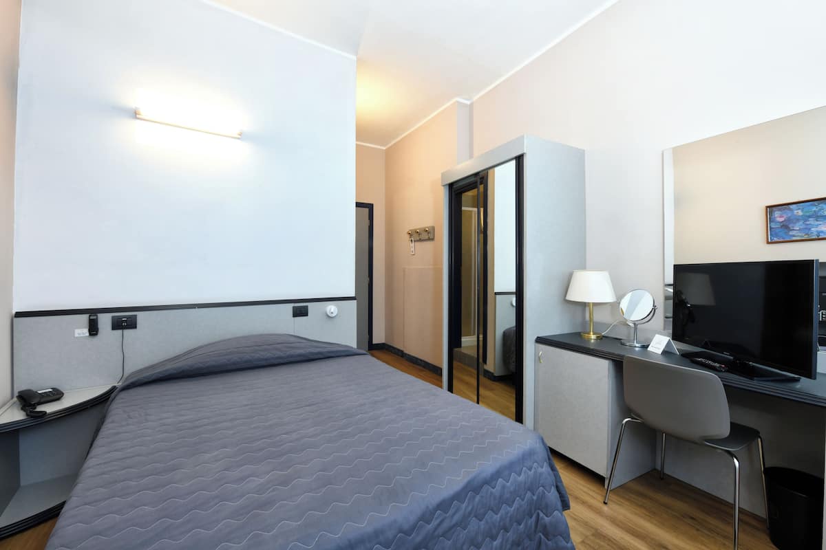 A hotel room with a bed, desk, chair, TV, and a mirror.