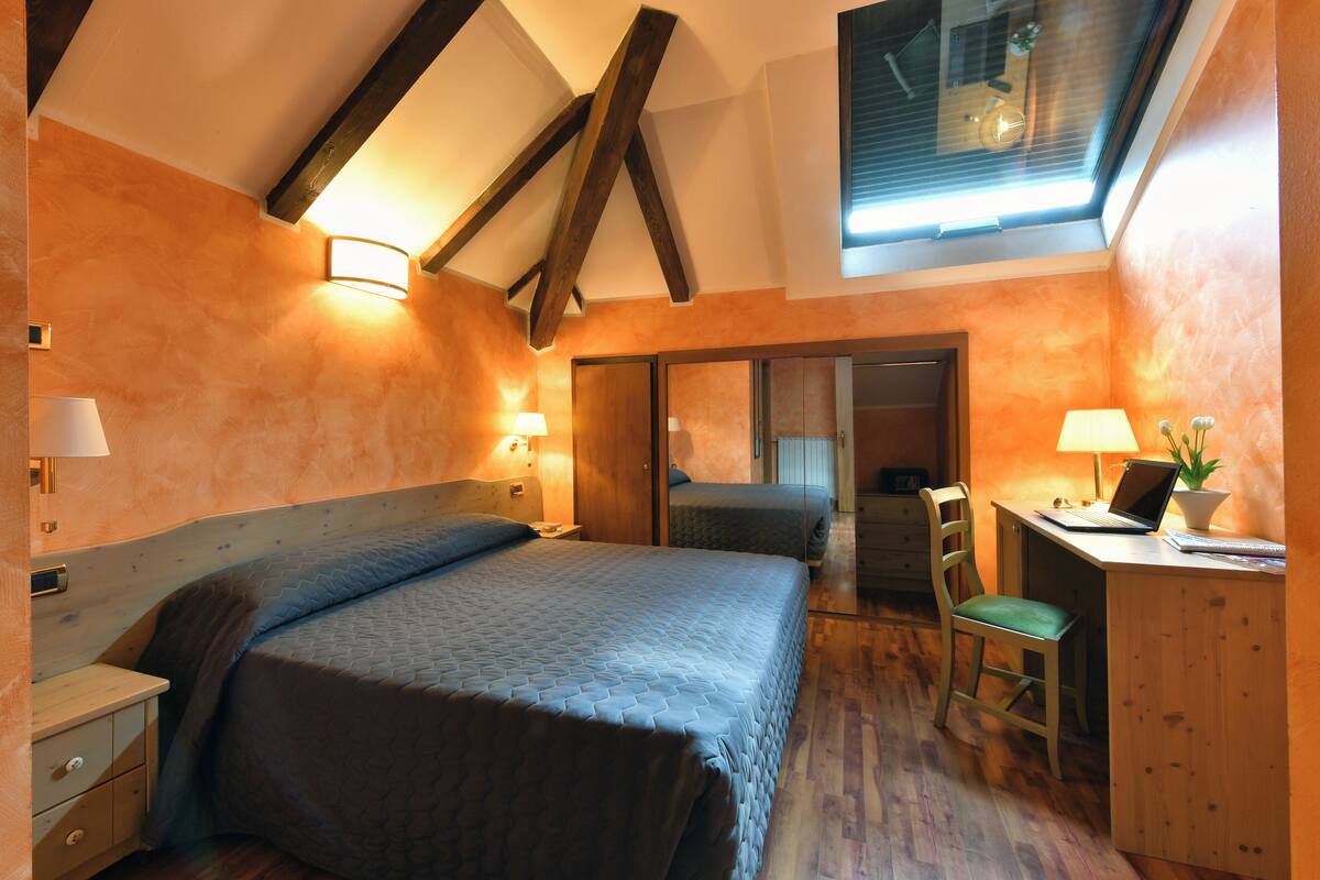 A bedroom with a bed, desk, chair, and a skylight.