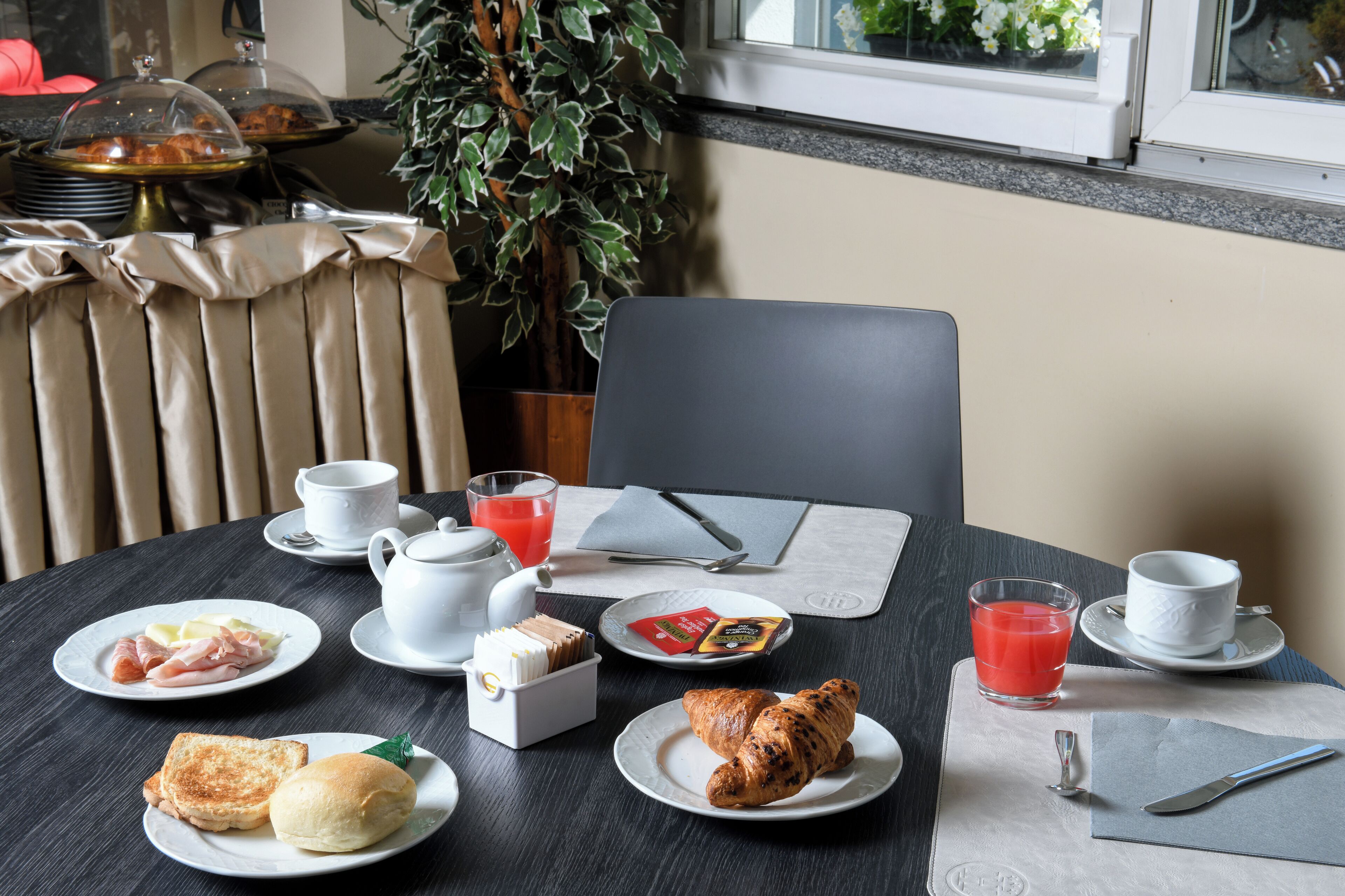 Une table de petit-déjeuner avec des assiettes remplies de nourriture, des tasses et une plante.