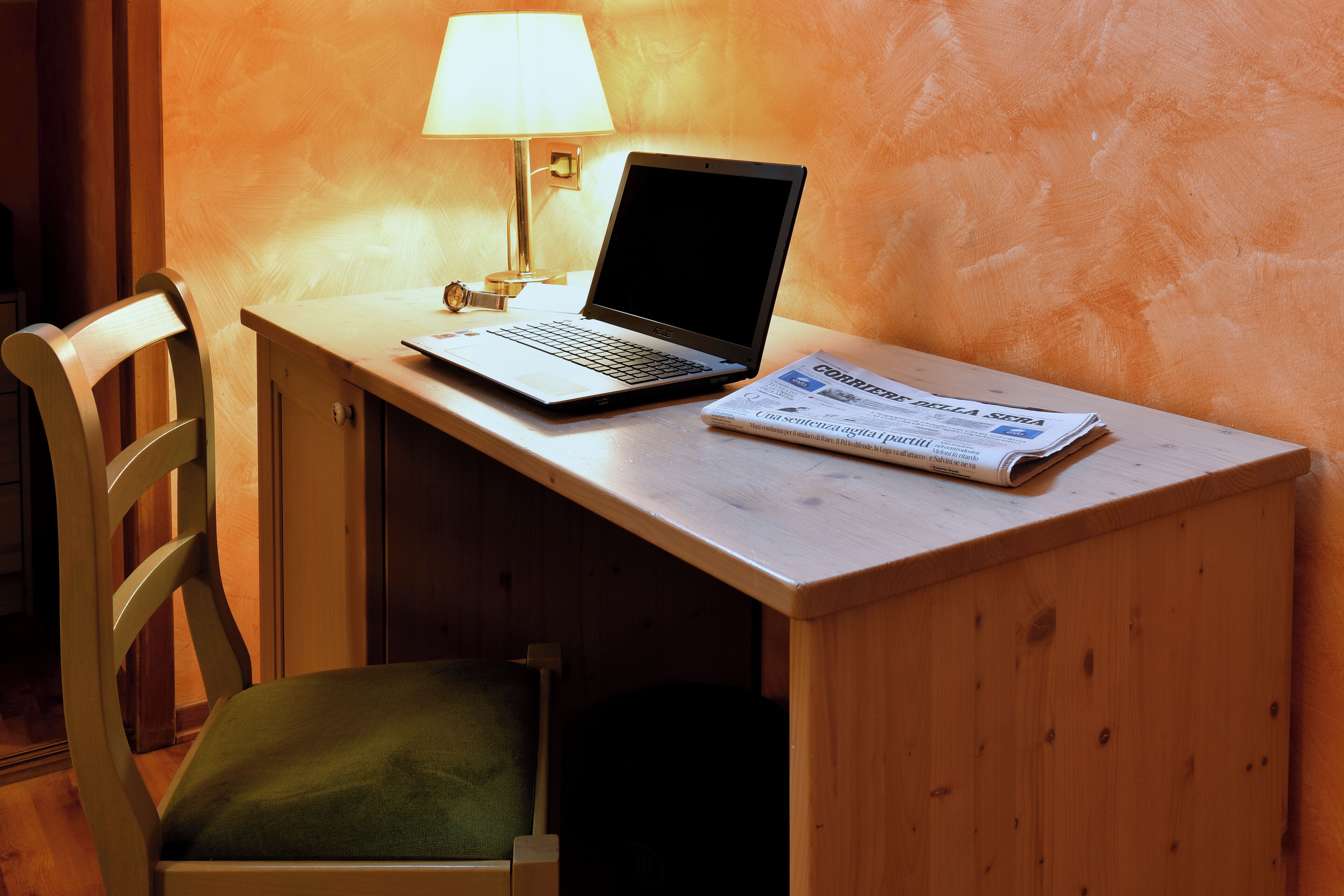 A wooden desk with a laptop and a newspaper.