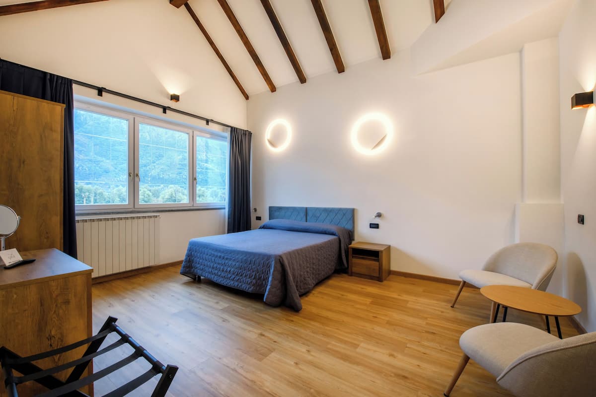 A modern bedroom with a large bed, wooden floor, a desk, and a chair. There are two bedside tables and a window with curtains.