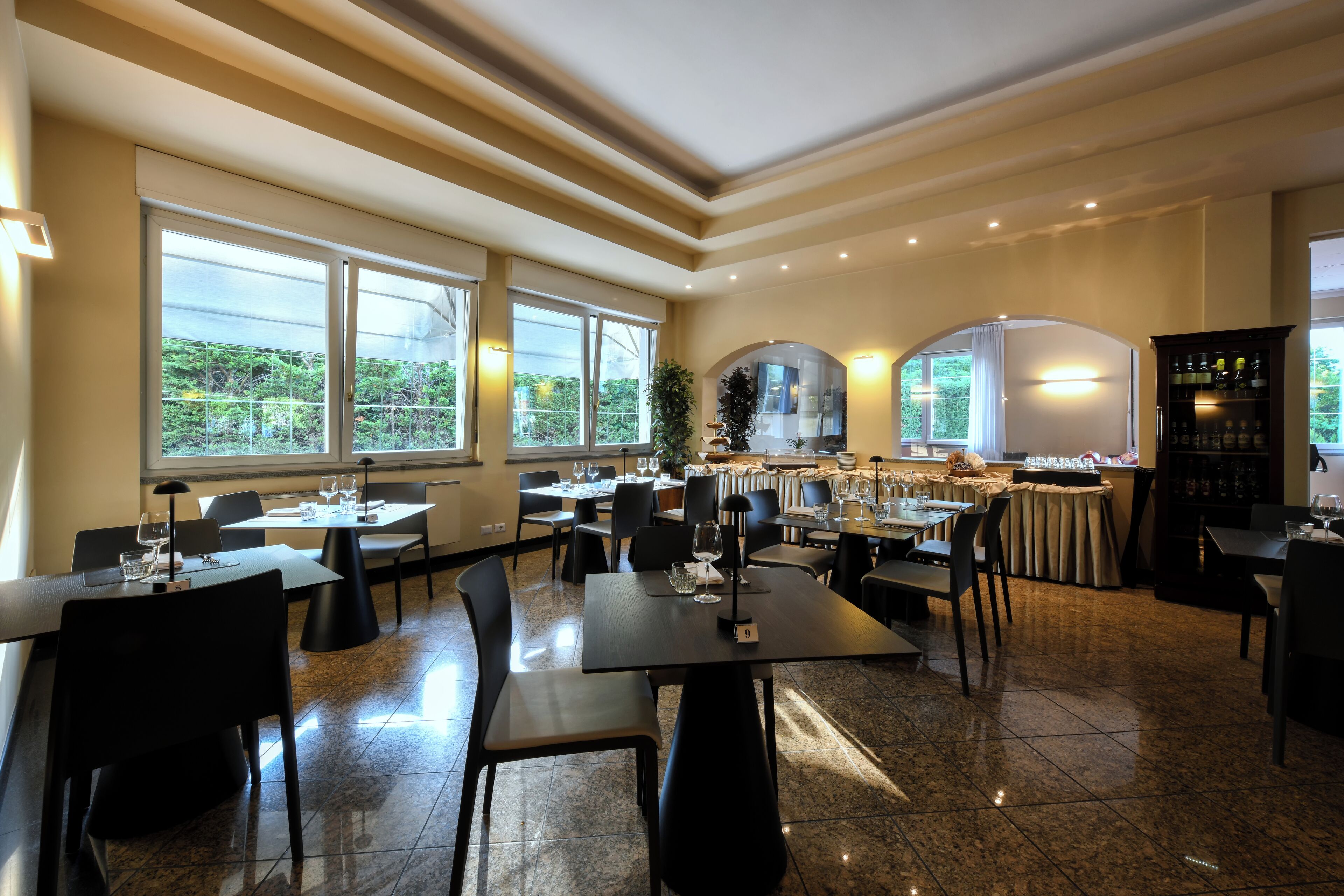 Un restaurante con varias mesas y sillas, amplios ventanales y una zona de bar.