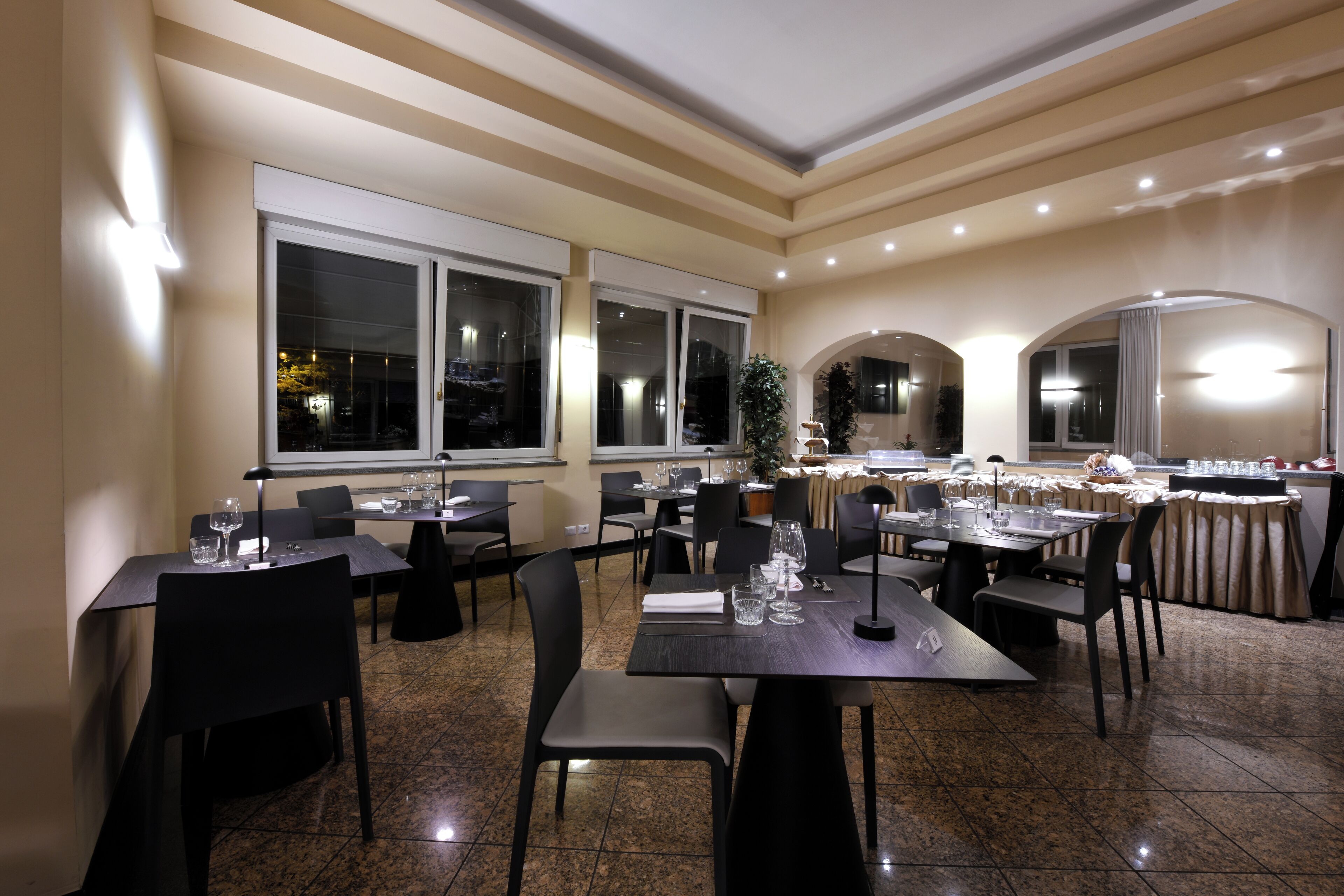 Un restaurant doté de nombreuses tables et chaises, de grandes fenêtres et d’un lustre.