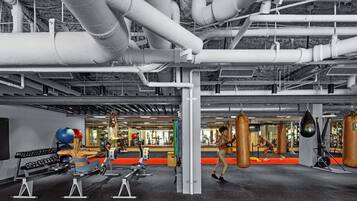 Een fitnessruimte met trainingsapparatuur, bokszakken en een rode loper.