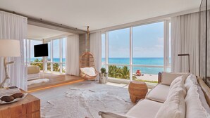 Un salón espacioso con un amplio ventanal con vistas a la playa, un sofá cómodo, una mesa de centro de madera y una silla de mimbre.