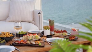 Una mesa de comedor con diversos platos y bebidas, un sofá y vista al océano.