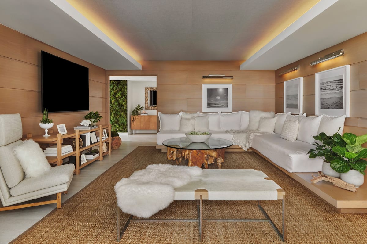 A modern living room with a sectional sofa, a glass coffee table, and a flat-screen TV mounted on the wall.