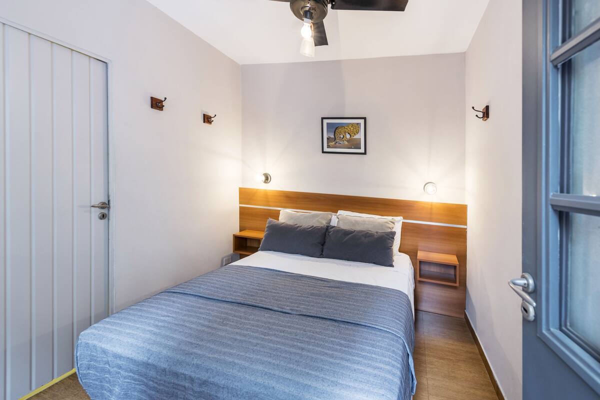 A bedroom with a bed, a wooden headboard, bedside tables, a ceiling fan, and a window.