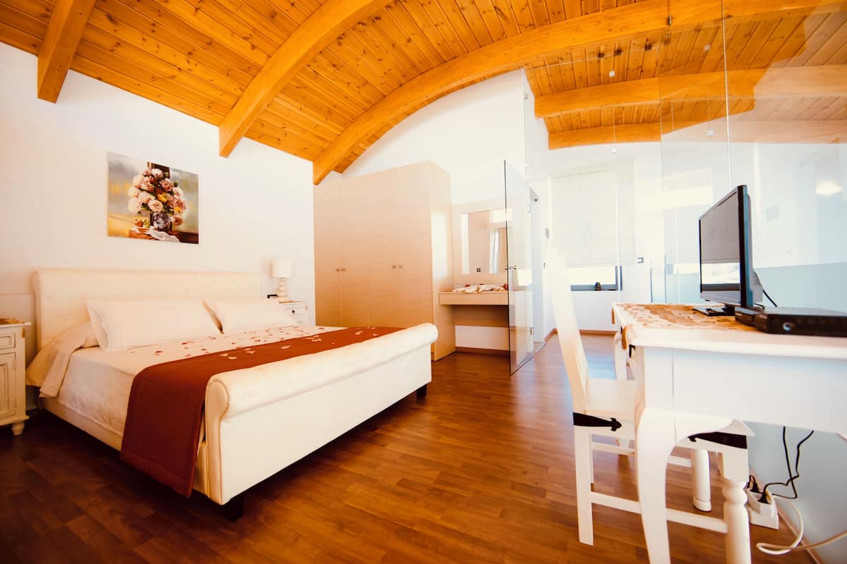 Un dormitorio con techo de madera, una cama con una manta marrón, un escritorio con una computadora y un espejo.