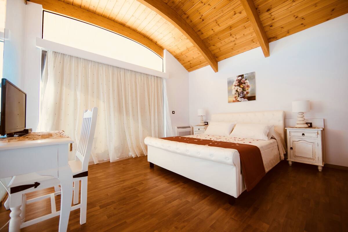 Un dormitorio con techo de madera, una cama, un escritorio y una silla.