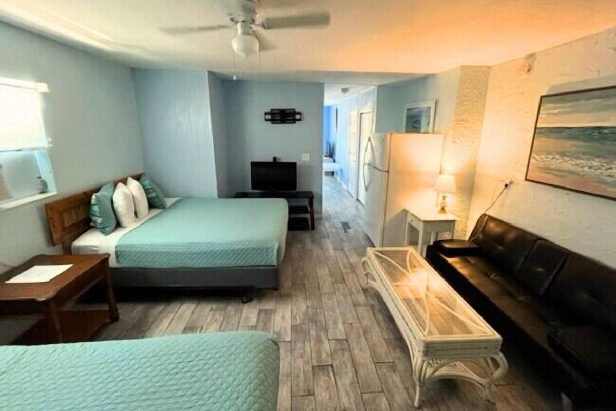 A bedroom with two beds, a ceiling fan, a TV, and a desk with a lamp.