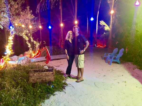 Two people standing in a sandy area with a wooden sign that reads "WELCOME". - Conch Key Fishing Lodge and Marina (Marathon)