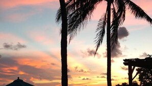 A sunset view with palm trees and a wooden deck with lounge chairs. - Conch Key Fishing Lodge and Marina (Marathon)