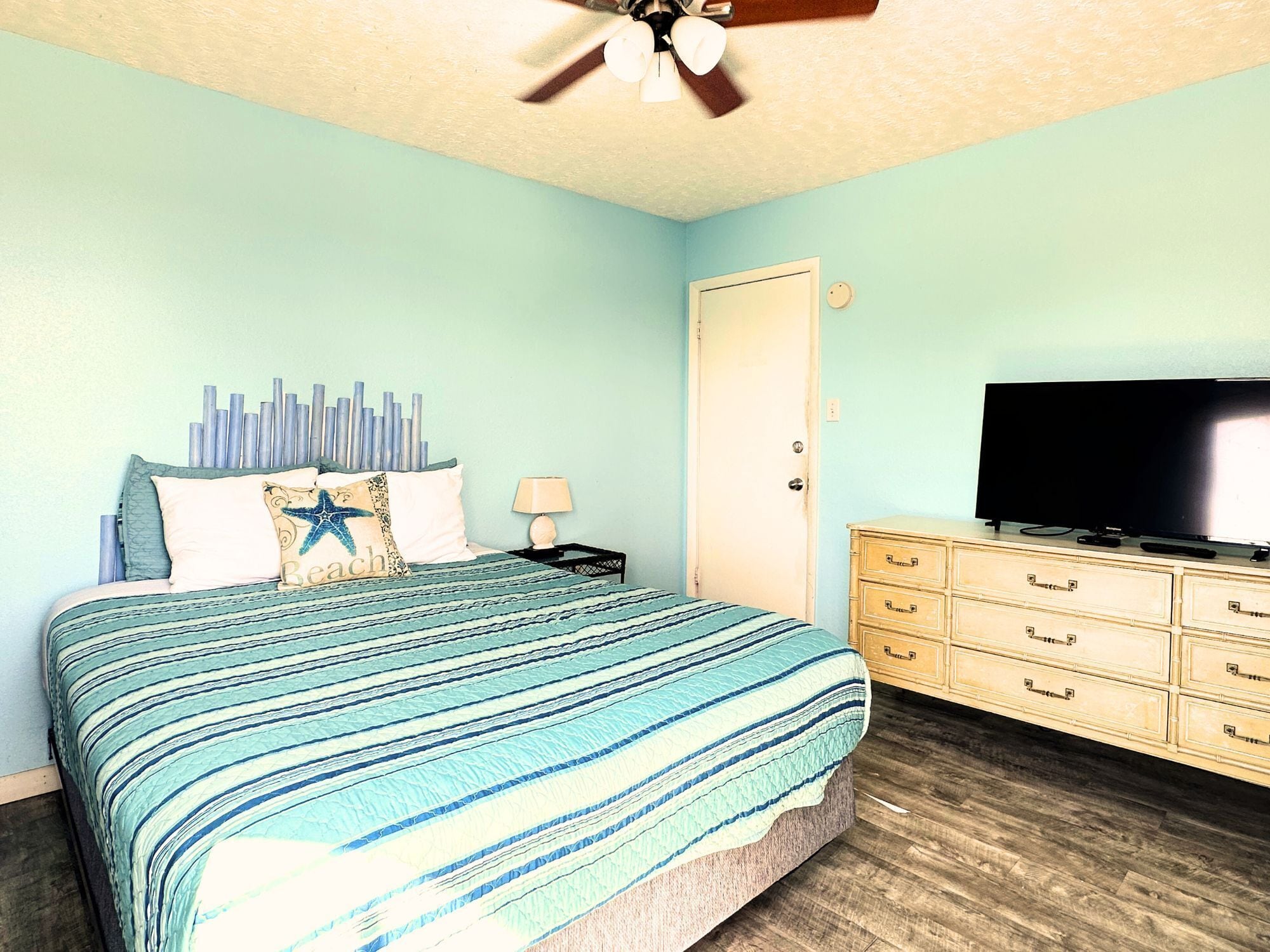 Un dormitorio con cama, cómoda, televisor y ventilador de techo.