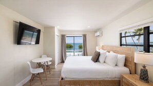 A hotel room with a bed, a TV, a balcony with a view of the sea, and a table with chairs. - Conch Key Fishing Lodge and Marina (Marathon)