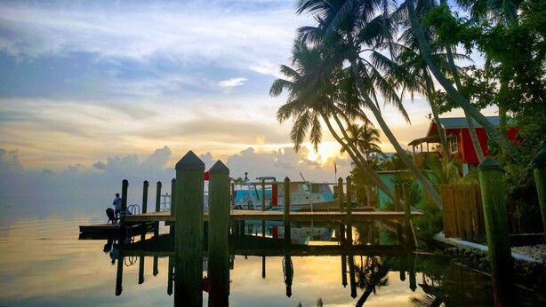 A dock with boats, a wooden pier, and a red building with a white window. - Conch Key Fishing Lodge and Marina (Marathon)