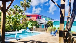 A pool area with a wooden deck, lounge chairs, and a building with a red and blue facade in the background. - Conch Key Fishing Lodge and Marina (Marathon)
