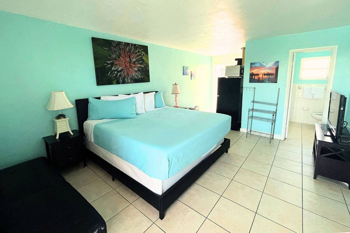 A hotel room with a bed, a desk, a chair, a TV, and a bathroom.