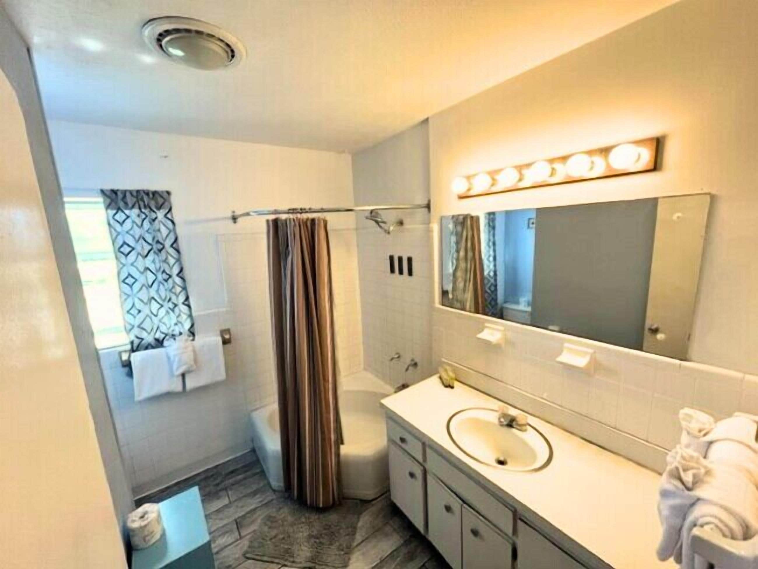 Un baño moderno con ducha, inodoro, tocador y un espejo grande con iluminación.
