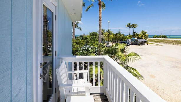 A beachfront property with a white balcony, palm trees, and a sandy beach. - Conch Key Fishing Lodge and Marina (Marathon)