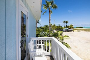 A beachfront property with a white balcony, palm trees, and a sandy beach. - Conch Key Fishing Lodge and Marina (Marathon)