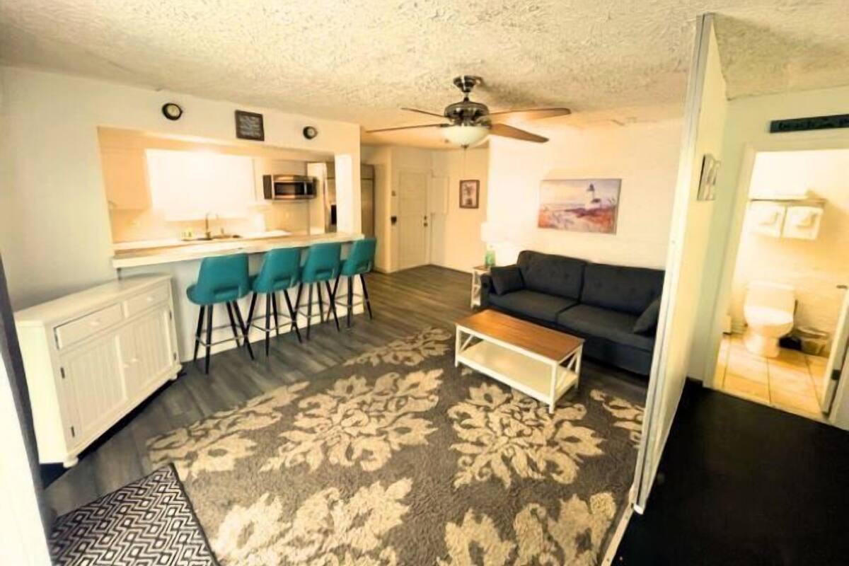 A compact living space with a kitchenette, a sofa, a coffee table, and a patterned rug.