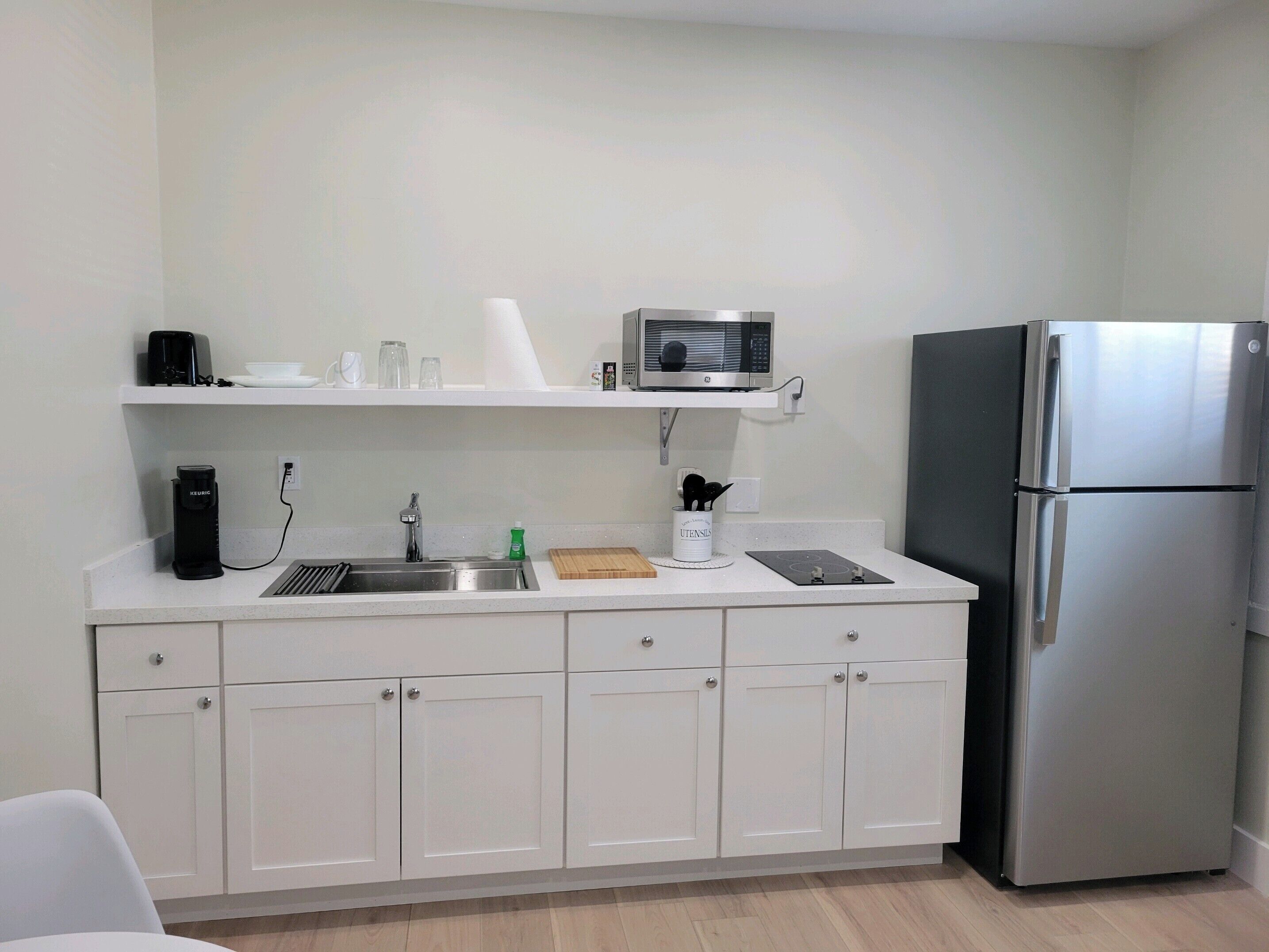 A modern kitchen with white cabinets, a stainless steel refrigerator, a microwave, and a coffee maker.