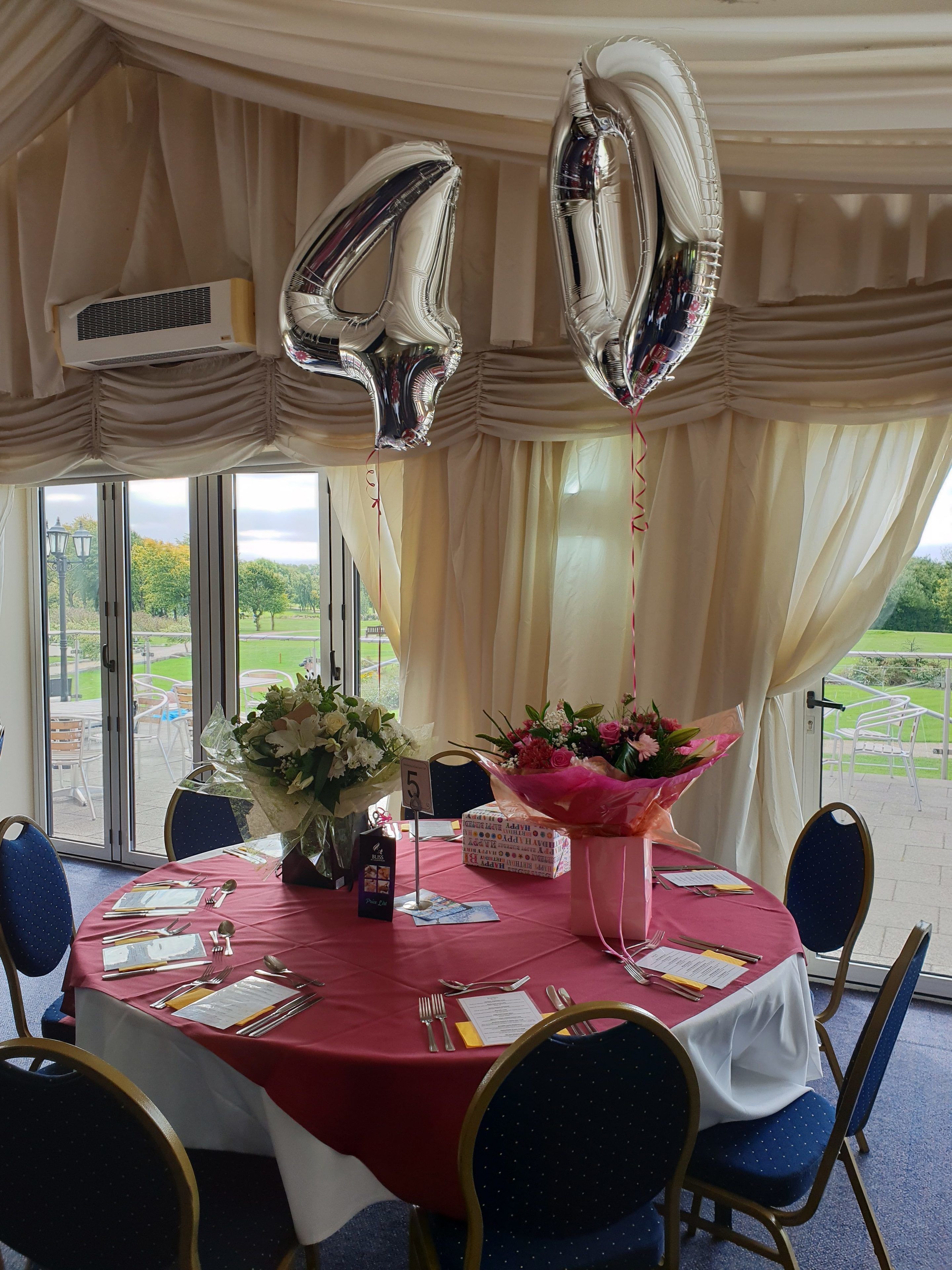 A round table with a red tablecloth, surrounded by chairs, and balloons shaped like the number 4.