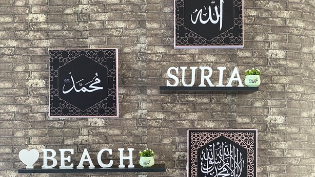 A wall with four framed signs and two potted plants. The signs display Arabic calligraphy and the words "SURIA" and "RESORT". - Suria Beach Resort (Pangkor Island)